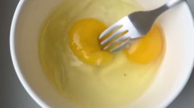 Stirring eggs with fork in white plate, close up. Cooking french omelette.