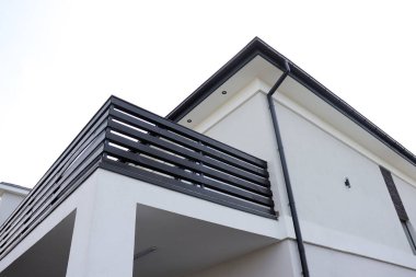 Beyaz yüzlü, balkonunda siyah korkuluğu olan modern bir özel ev. Temiz tasarım ve keskin çizgiler eve gösterişli, minimalist ve çağdaş bir görünüm kazandırıyor..