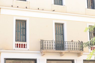 Yunanistan 'ın Heraklion kentindeki tarihi bir bina, krem rengi duvarlar, yeşil kepenkler zarif bir demir balkon ve korkuluklarda oturup sakin bir Akdeniz atmosferini yakalayan güvercinler..