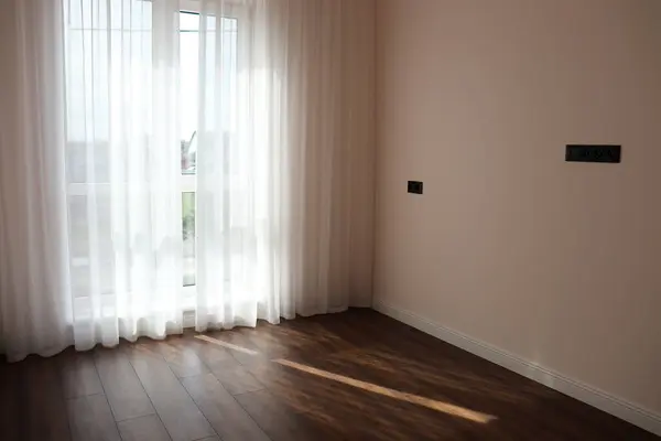  Pencereyi kaplayan saf beyaz perdeli parlak bir oda, içeri doğal ışık girmesini sağlıyor ve minimalist bir alanda yumuşak, huzurlu bir atmosfer yaratıyor..