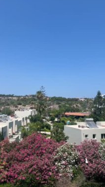 Ayia Napa, Kıbrıs - 6 Haziran 2023: Kıbrıs Rum Kesimi 'nin Ayia Napa kentindeki bir otelden manzara, beyaz binalar, çiçek açan bahçeler, yeşil palmiye ağaçları ve parlak mavi bir gökyüzünün altında manzaralı bir tepe.