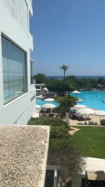 Ayia Napa, Kıbrıs - 5 Haziran 2023: Kıbrıs Rum Kesimi 'nin Ayia Napa kentinde açık bir gökyüzü altında beyaz şemsiyeler, yeşil çimenler ve mavi deniz ufkuyla lüks bir tatil beldesi manzarası.