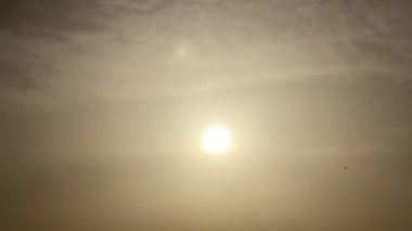 Güneşin sakin bir görüntüsü, altın rengi gökyüzünde hafif bir şekilde parıldıyor. Işık bulutları, sakin ve huzurlu bir atmosfer. Uzakta tek başına süzülür, bu sakin ve meditasyon sahnesine hayat katar.
