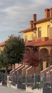 Pienza, İtalya - 24 Kasım 2024: Pienza 'da modern yerleşim alanı, sıcak sarı ve terakotta renkli evler, kırmızı kiremit çatılar, ve parçalı bulutlu gökyüzü altında düzgün bir şekilde korunan bahçeler.