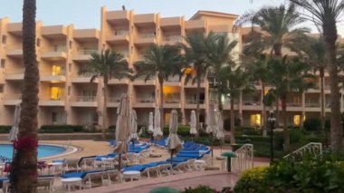 Hurghada, Mısır - 11 Kasım 2024: Tropik palmiye ağaçları ve geceleri yüzme havuzu olan otel, Hurghada, Mısır.