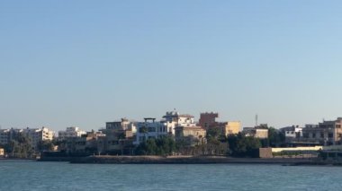 Hurghada, Mısır 'ın sakin kıyı manzarası. Sahil evleri, palmiye ağaçları ve berrak gökyüzünün altındaki sakin mavi deniz bu sahil kasabasının cazibesini yansıtıyor..