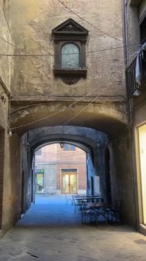 Siena, İtalya 'da dar bir sokak. İçinde yıpranmış taş duvarlar, kemerli bir geçit ve süslü bir mabet var. Konforlu kafe masaları cazibe, tarih ve modern hayatı harmanlıyor..
