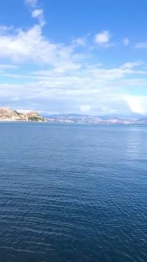 Korfu, Kerkyra 'da sakin deniz manzarası, sakin mavi sularda yüzen yelkenliler. Huzurlu ortam, parlak mavi gökyüzünün altında bir dağ zeminine sahip, güzel bir Akdeniz manzarası yaratıyor