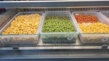 Bir dükkanda plastik kaplarda sergilenen farklı renkte ve şekillerde taze el yapımı makarna. Sarı, yeşil ve turuncu makarna çeşitleri. Doğal malzemelerle yapılmış, pişirmeye hazır..