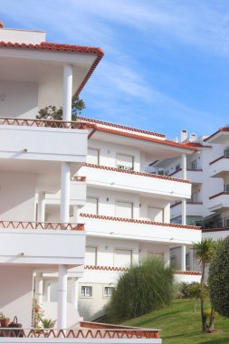 Ericeira, Portekiz 'de güzel beyaz bir Akdeniz tarzı apartman kompleksi. Binaların kırmızı kiremitli çatıları, geniş balkonları ve yemyeşil bir bahçesi var..
