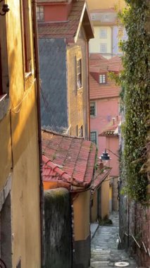 Günbatımında Portekiz, Porto 'da rahat bir sokak manzarası. Taştan duvarların arasında kırmızı kiremitli çatıları olan eski evler nehir kenarındaki renkli binalara çıkıyor.. 