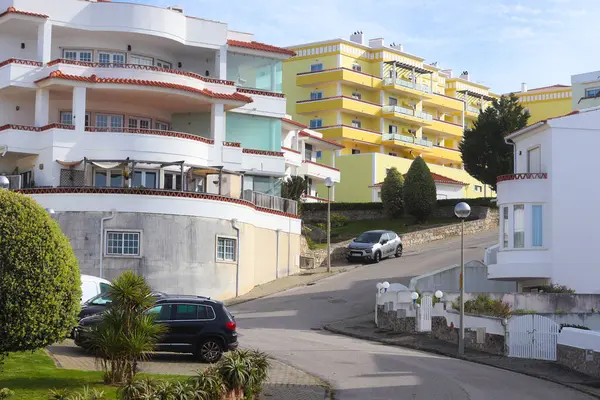 Ericeira, Portekiz - 24 Şubat 2025: Modern beyaz ve sarı apartman binaları, sakin sokaklar ve kıyı kasabasındaki Akdeniz bitkilerine sahip güneşli meskun bölge.