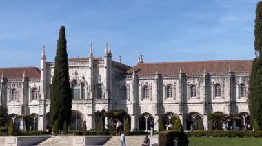 Lizbon, Portekiz - 23 Şubat 2025: Güneşli bir günde Lizbon 'daki Jernimos Manastırı. Ön planda ağaçlar ve ziyaretçiler tarafından çevrelenmiş ayrıntılı cepheli gotik mimari..