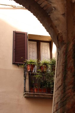 İtalya, Montepulciano 'da büyüleyici bir balkon, kemer yolu ile çerçevelenmiş, sıcak İtalyan güneşinin altındaki korkulukları kaplayan saksı bitkileriyle.
