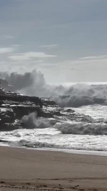 Güçlü okyanus dalgaları Praia do Norte, Portekiz 'in kayalıklarına çarpıyor ve üzerinde ünlü deniz feneri duruyor. Dramatik gökyüzü ve sisli hava nefes kesici bir kıyı manzarası yaratır..