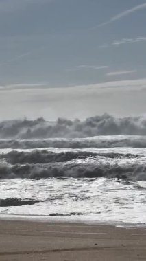 Güçlü okyanus dalgaları, Portekiz, Nazar 'da parçalı bulutlu bir gökyüzünün altında kumlu sahile çarpıyor ve Atlantik kıyısının dinamik güzelliğini gösteriyor..
