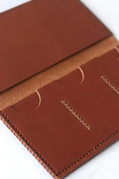 Kart yuvaları olan el yapımı kahverengi deri cüzdan, minimal tasarım ve görünür dikişler. Hafif bir arkaplanda zarif bir aksesuar fotoğrafı..