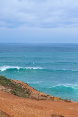 Nazar kıyı şeridinin kayalık manzarası kasvetli bir gökyüzü altında güçlü okyanus dalgaları Portekiz Atlantik kıyılarının saf güzelliğini yakalıyor..