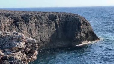Berrak mavi suyu olan engebeli bir sahil kayalığı, parlak bir gökyüzüne karşı kurulmuş, Kaptan d Artrutx, Menorca 'nın doğal güzelliğini gözler önüne seriyor..
