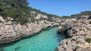İspanya 'nın Menorca kentindeki gizli bir koy olan Cala en Brut' ta kayalık kayalıklar ve yemyeşil yeşilliklerle çevrili kristal berraklığında turkuaz sular bulunuyor. Yüzmek ve huzur içinde dinlenmek için ideal..