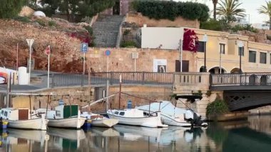 Port de Ciutadella 'da sakin bir akşam, sakin sulara yanaşmış teknelerle. Sahne, Akdeniz mimarisi ve palmiye ağaçlarıyla çevrili manzaralı bir alana çıkan bir merdiveni içeriyor..