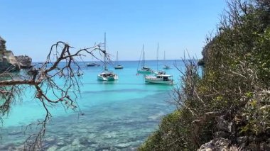 Cala Macarella, Menorca 'nın kristal berraklığında demirlemiş yelkenliler, güneşli bir yaz gününde kireçtaşı kayalıkları ve bereketli Akdeniz bitkileriyle çevrili..