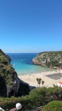 Cala en Porter, Menorca 'da sakin bir sahil manzarası, turkuaz sular, kumlu kıyılar, ve berrak mavi gökyüzü, tatil, rahatlama ve kıyı görüntülemesi için ideal..