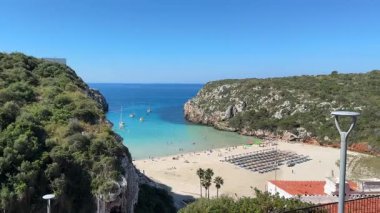Cala en Porter, Menorca 'da sakin bir sahil manzarası, turkuaz sular, kumlu kıyılar, ve berrak mavi gökyüzü, tatil, rahatlama ve kıyı görüntülemesi için ideal..