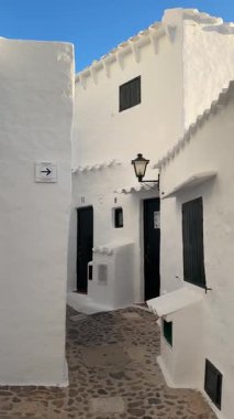 Geleneksel beyazlatılmış binibeca Vell, Menorca evleri, panjurları ve mavi gökyüzünün altında ahşap balkonları var. Huzurlu mimarisi olan büyüleyici bir Akdeniz köyü..