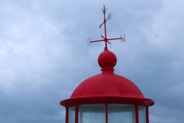 A red lighthouse at Forte de Sao Miguel Arcanjo in Nazare, Portugal. The historic beacon stands against a cloudy sky, overlooking the Atlantic Ocean, guiding sailors near the famous big wave surf spot