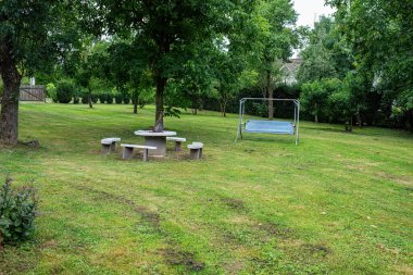 Tahta şöminesi ve ağaçların altındaki bankları olan yeşil bir bahçe ve dışarıda dinlenmek için sallanan bir koltuk. Yaz tatili için mükemmel bir bahçe..