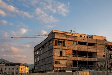 Gün batımında kule vinci olan inşaat ya da yenileme halindeki bir şehir binası. Sahne, bir inşaat alanının endüstriyel atmosferini modern gelişim ve çevre şehir mimarisi arasında bir kontrastla yakalıyor..