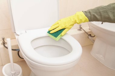 Koruyucu sarı eldivenli, yeşil süngerli kadın elleri. Tuvaleti ev yapımı kimyasallarla temizliyor. Tuvalet temizliği, dezenfeksiyon ve hijyen konsepti