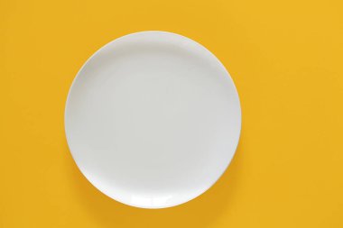 Sarı arka planda boş beyaz seramik plaka. Üst görünüm, boşluğu kopyala. Bahar ve Yaz Menüsü