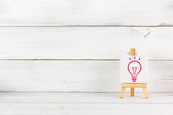 stock image Red Light Bulb Icon on Wooden Easel: Concept of Innovation and Bright Ideas