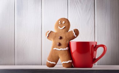 Smiling Gingerbread Man Cookie with Red Mug Against Clean White Background clipart