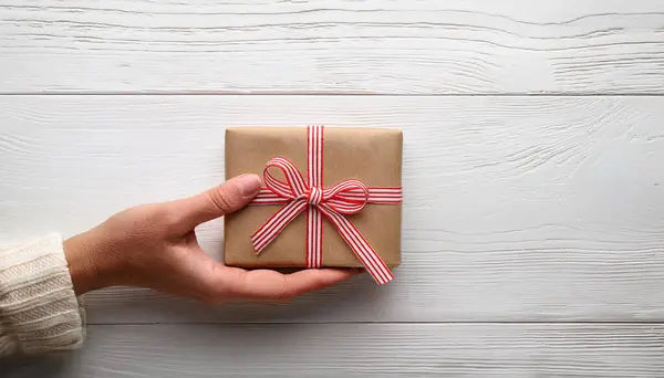 stock image Hand Holding Gift Box with Red Ribbon on Minimal Wooden Background for Special Occasions