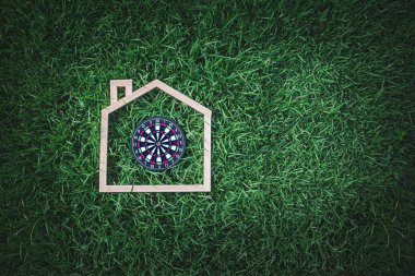 Dartboard Positioned Inside Wooden House Outline on Green Grass Representing Focus and Strategy in Home Life clipart