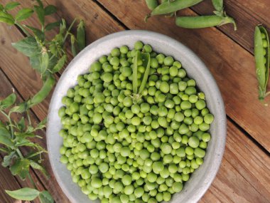 Tabakta taze yeşil bezelyeler, ahşap bir masa, üst manzara.