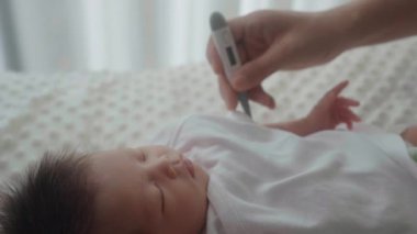 Anne, bebeğin ısısını dijital termometreyle ölçer.