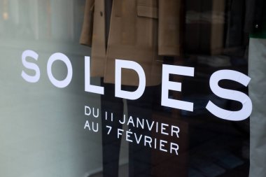 Closeup of discount sign SOLDES du 11 janvier au 7 fevrier  in french,  the traduction of  sales from January 11 to February 7  in english on the window of fashion store 