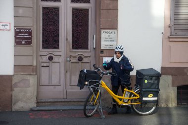 Mulhouse - France - 7 February 2023 - Portrait of french post woman and bicycle standing in the street