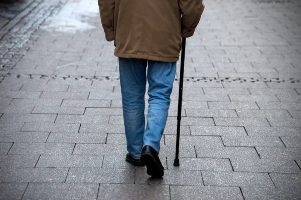 Closeup of legs of old man waking in the street with stick