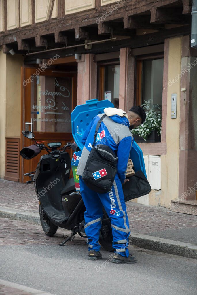 Colmar - France - 30 April 2023 - Portrait of dominos pizza delivery man with scooter in the street