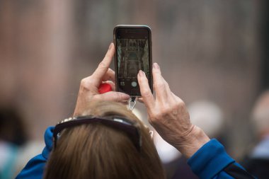 Sokakta akıllı telefonuyla fotoğraf çeken yaşlı bir kadının elleri yakın plan.