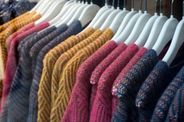Kadın moda mağazasındaki askılarda asılı renkli yün kazakların yakın çekimi.