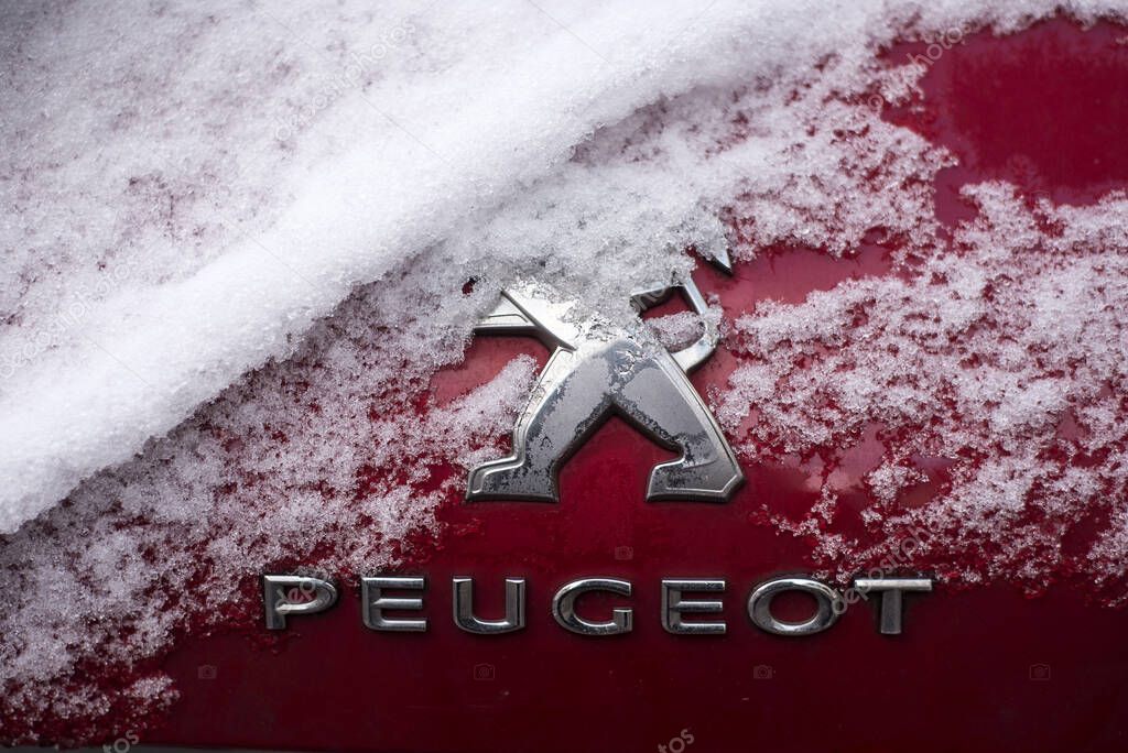 Mulhouse - France - 19 January 2024 - Closeup of Peugeot logo covered by the snow on red car parked in the street