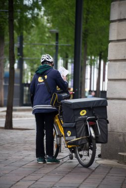 Mulhouse - Fransa - 14 Nisan 2024 - Sokakta bisikletinin yanında duran postacının portresi