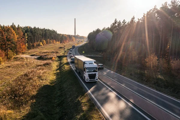 Truck is driving through the forest in autumn. Truck with semi-trailer in gray color. Car transport .