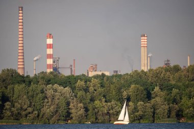 Endüstriyel çelik fabrikası, demir işi. Metalürjik bitki. Çelik fabrikası. Avrupa 'da ağır sanayi. Bacalardan gelen hava kirliliği. Mavi Göl 'ün arka planında demir işçiliği. Doğa ve endüstri.